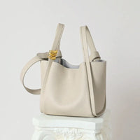 Beige leather tote bag with gold accent on strap, minimalist style, on decorative pedestal