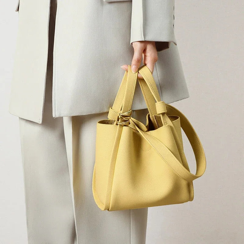 Woman in beige suit holding small yellow leather bucket bag