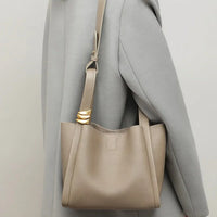 Taupe leather shoulder bag with gold accent on strap worn over gray coat