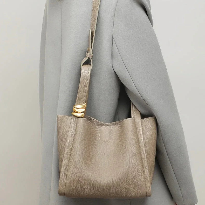 Taupe leather shoulder bag with gold accent on strap worn over gray coat