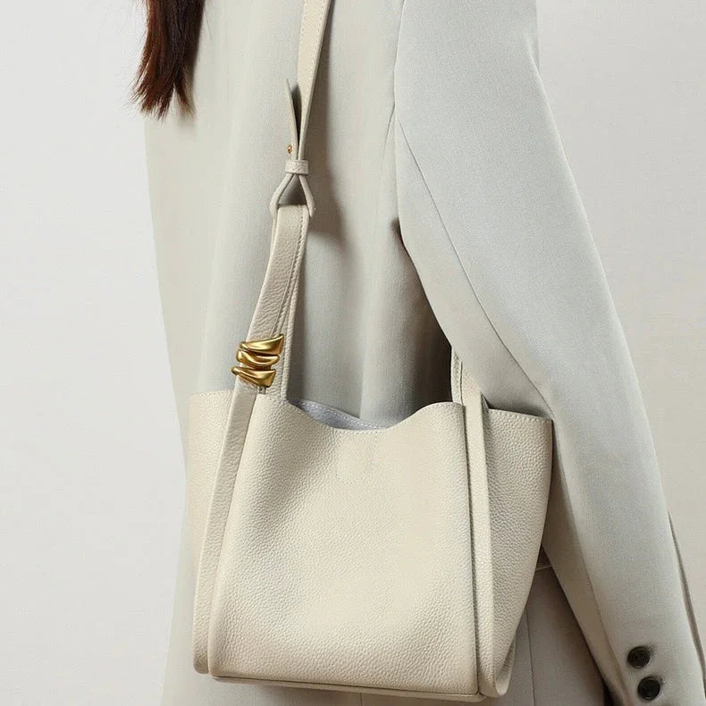 Woman in light blazer carrying a cream leather shoulder bag with gold accent detail