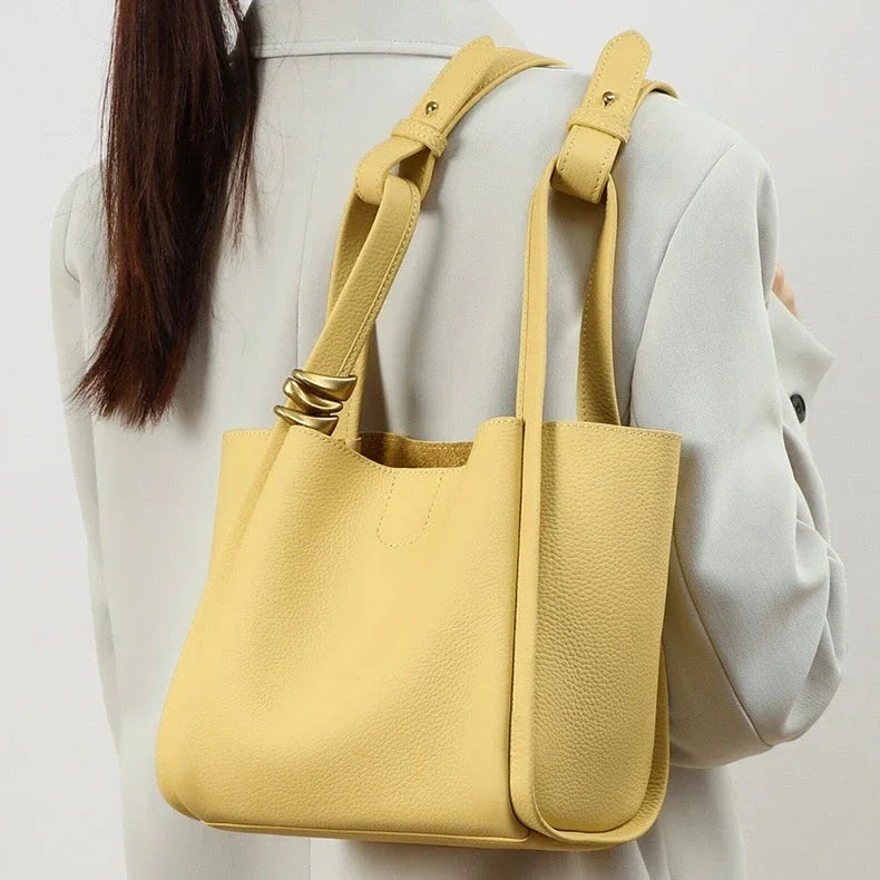 Yellow leather tote bag with gold rings on strap, worn over a light blazer
