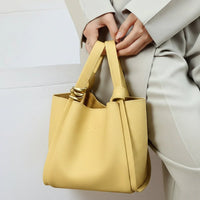 Woman in light suit holding a yellow leather handbag with gold ring accents