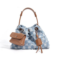 Blue and white checkered denim handbag with tan leather handle and pouch, white background