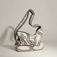 Patterned canvas shoulder bag with black and white chain design on a wooden cane chair