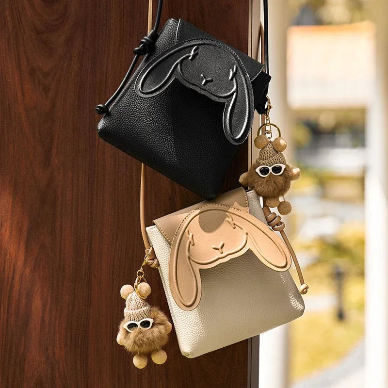 Black and beige bunny crossbody bags with cute keychains hanging on a wooden door