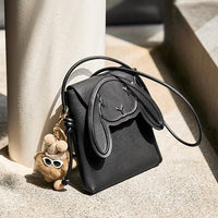 Black leather bunny ear crossbody bag with plush bear keychain on stone steps