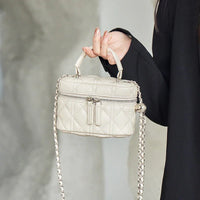 Quilted cream mini handbag with chain strap and zipper, held by woman in black sleeve