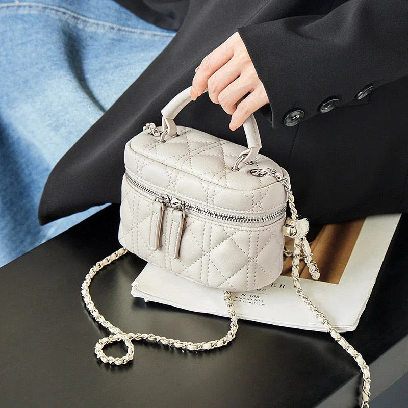 Quilted beige mini handbag with chain strap held by person in black blazer, on magazine