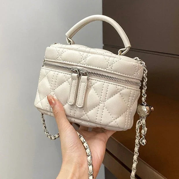 Hand holding a small quilted white leather handbag with chain strap and top handle