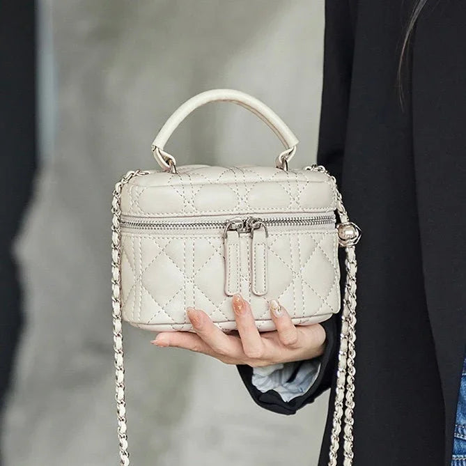 Elegant quilted beige mini handbag with top handle and chain strap, held by a woman