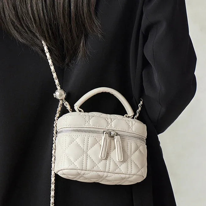 Quilted ivory mini crossbody bag with top handle and zipper, worn on black outfit
