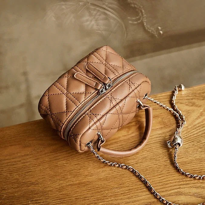 Quilted brown leather handbag with chain strap on wooden table
