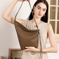 Woman holding large brown leather shoulder bag in minimalist indoor setting