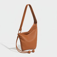 Brown leather shoulder bag with adjustable strap and ball tassel accents on white background.
