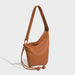 Brown leather shoulder bag with adjustable strap and ball tassel accents on white background.