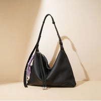 Black leather hobo bag with adjustable strap and lilac accent cord on beige background