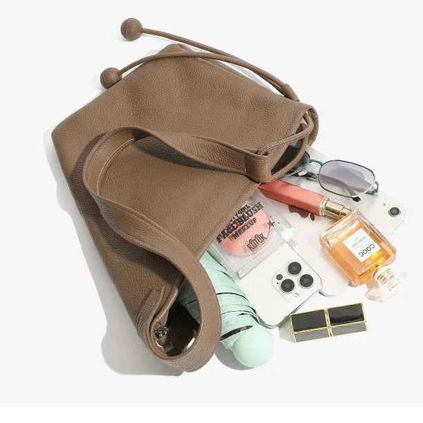 Brown leather tote bag with makeup, sunglasses, perfume, and phone on white background