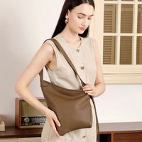 Woman in beige dress holding brown leather shoulder bag indoors