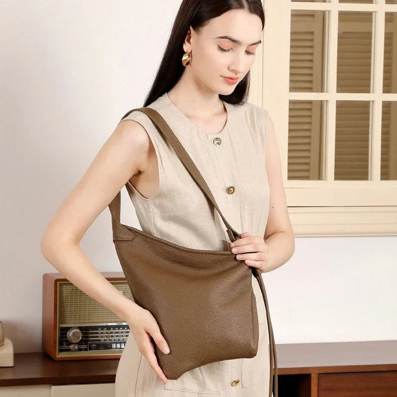 Woman in beige dress holding brown leather shoulder bag indoors