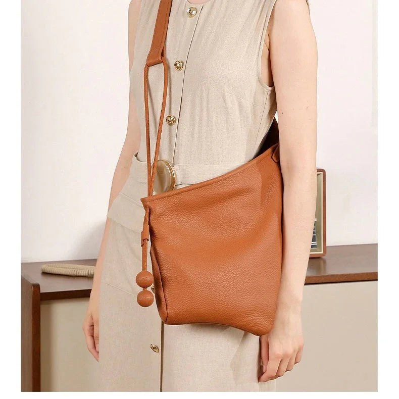 Woman in beige dress carrying a brown leather shoulder bag with decorative tassels
