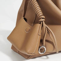 Tan pebbled leather handbag with drawstring, metal ring, and decorative stitching