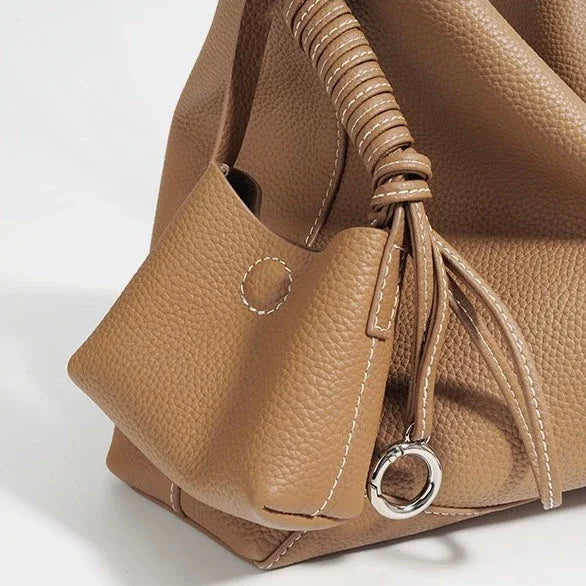 Tan pebbled leather handbag with drawstring, metal ring, and decorative stitching