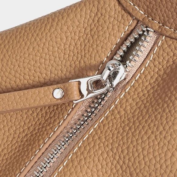 Close-up of tan leather bag with silver zipper and textured stitching detail