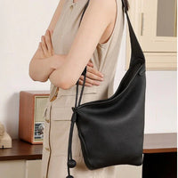Woman wearing sleeveless beige dress with large black leather shoulder bag indoors