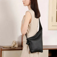 Woman in beige dress carrying a black leather crossbody bag indoors by a vintage phone