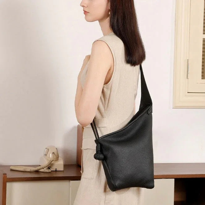 Woman in beige dress carrying a black leather crossbody bag indoors by a vintage phone