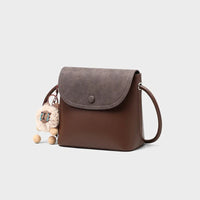 Brown crossbody bag with gray flap and plush keychain, minimalist white background