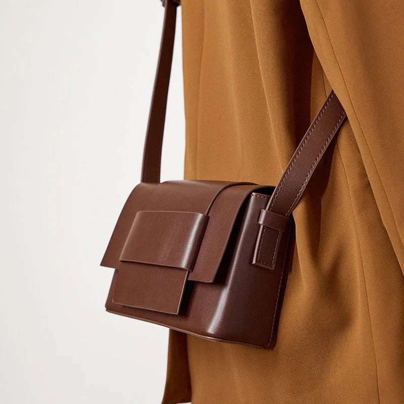 Minimalist brown leather crossbody bag on tan coat