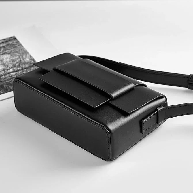 Minimalist black leather crossbody bag with rectangular shape on white background