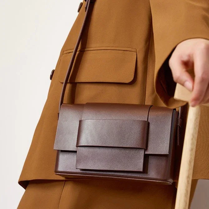 Brown leather crossbody bag worn with tan suit jacket, modern minimalist style