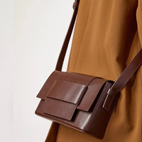 Brown leather crossbody bag with flap on person wearing tan outfit