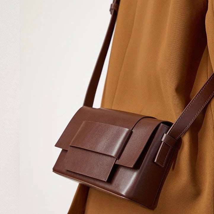 Brown leather crossbody bag with flap on person wearing tan outfit