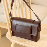 Brown leather shoulder bag on wooden chair, minimalist design, crossbody purse
