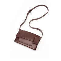 Minimalist brown leather crossbody bag with adjustable strap on white background