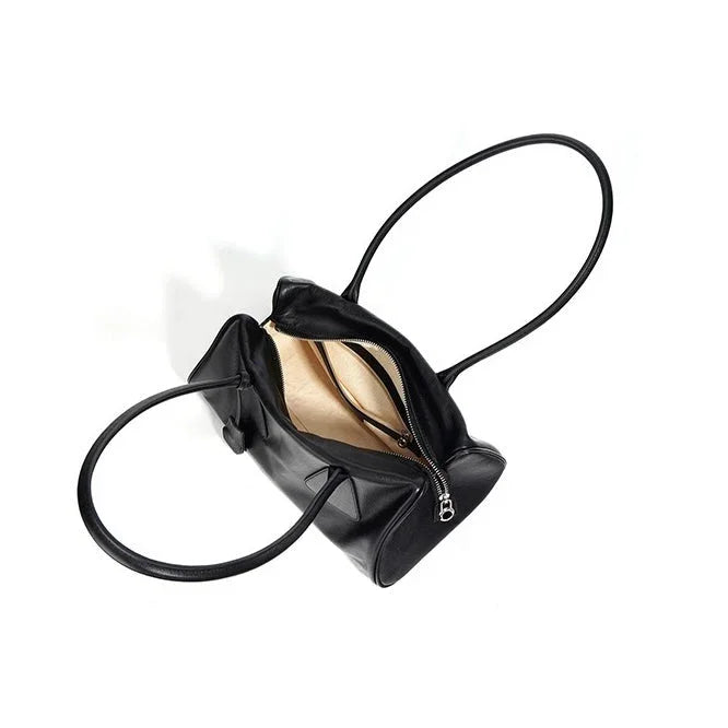 Black leather handbag with zippered opening and beige interior on white background