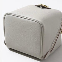 Minimalist light gray leather box purse with zipper and gold clasp on white background
