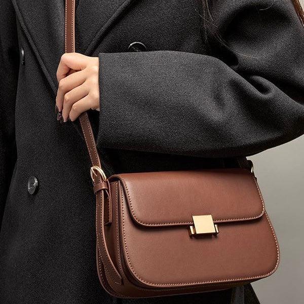 Woman wearing dark coat holding brown leather crossbody bag with gold clasp