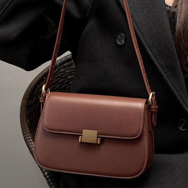 Brown leather crossbody bag with gold clasp on woman in black coat