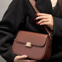 Woman in black coat holding stylish brown leather crossbody bag with gold clasp