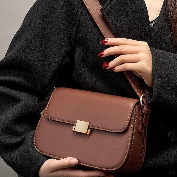 Woman in black coat holding stylish brown leather crossbody bag with gold clasp