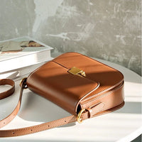 Brown leather crossbody bag with gold buckle on table, fashion accessory