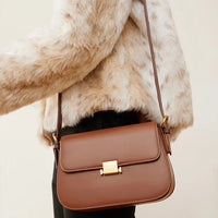 Brown leather crossbody bag with gold clasp worn over faux fur jacket