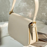 Beige leather shoulder bag with gold buckle details on a marble surface