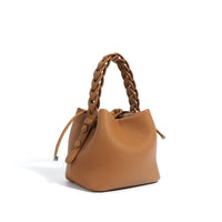 Brown leather bucket bag with braided handle and drawstring closure on white background