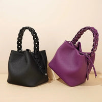 Black and purple leather handbags with braided handles on beige background